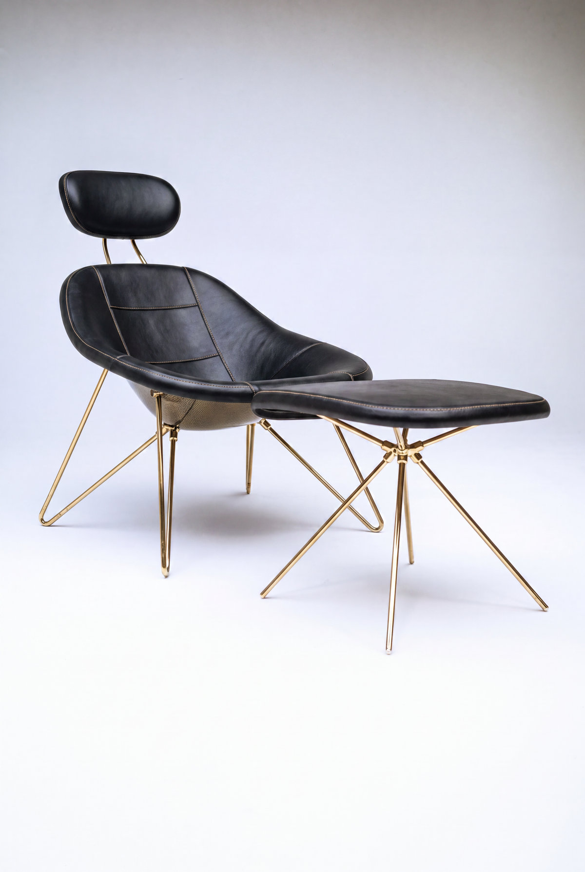 House Dé Stains bespoke automotive furniture: Three-quarter view of the Maniac Lounge Chair and matching ottoman featuring black leather upholstery, a structural carbon fiber shell, and polished gold-finished tubular steel frames.