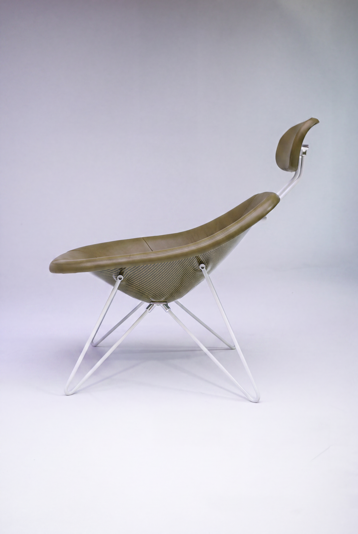 House Dé Stains bespoke automotive furniture: Profile view of the Maniac Lounge Chair featuring olive green upholstery, a glossy carbon fiber composite shell, and a custom white tubular steel frame.