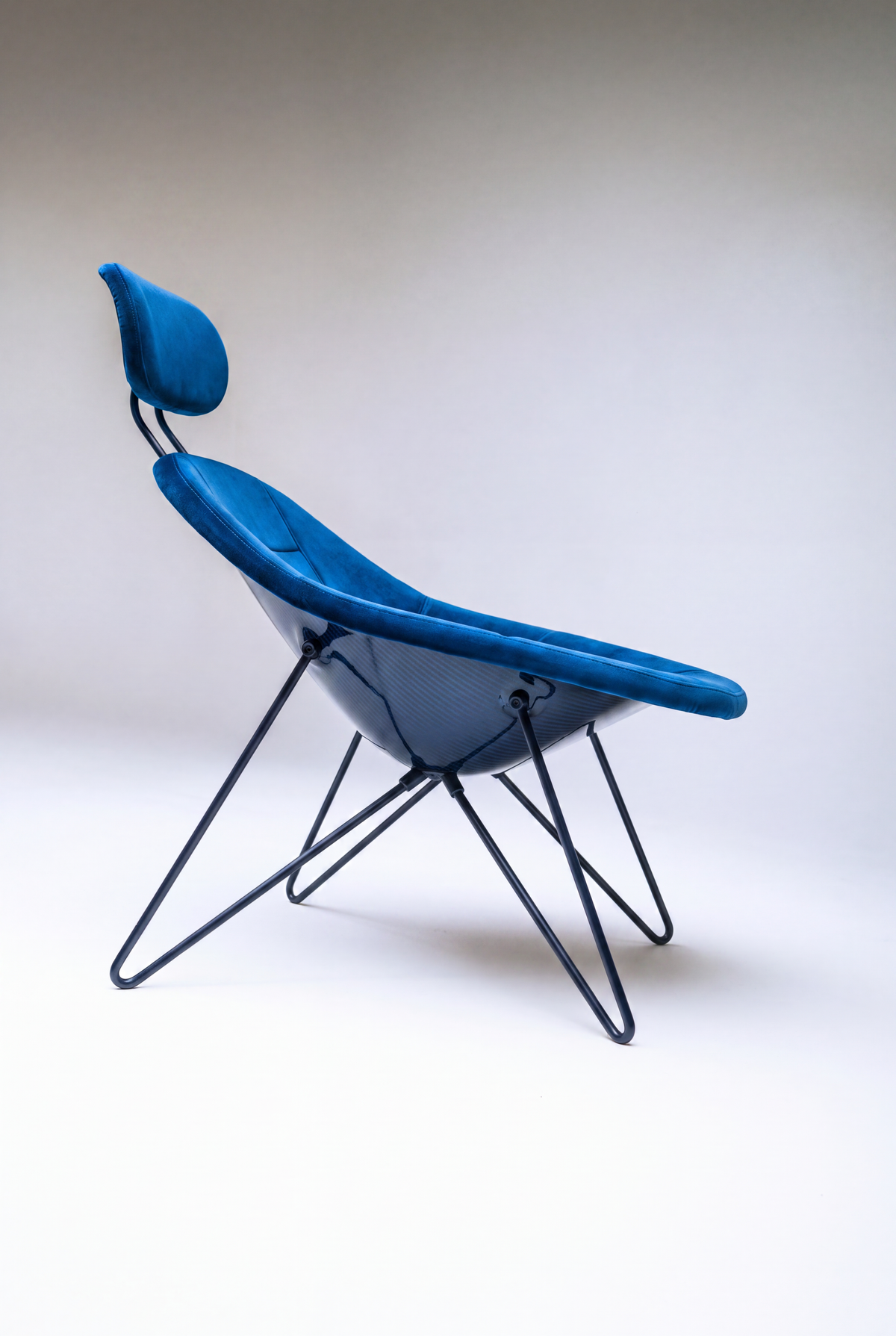 House Dé Stains bespoke automotive furniture: Profile view of the Maniac Chair featuring vibrant blue upholstery, a glossy hand-finished carbon fiber composite shell, and a black tubular steel wire frame.